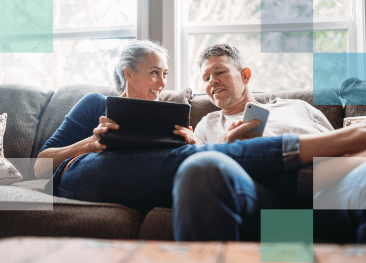 Older man and woman sitting on the couch with mobile and tablet technology smiling