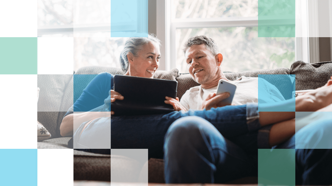 Older man and woman sitting on the couch with mobile and tablet technology smiling