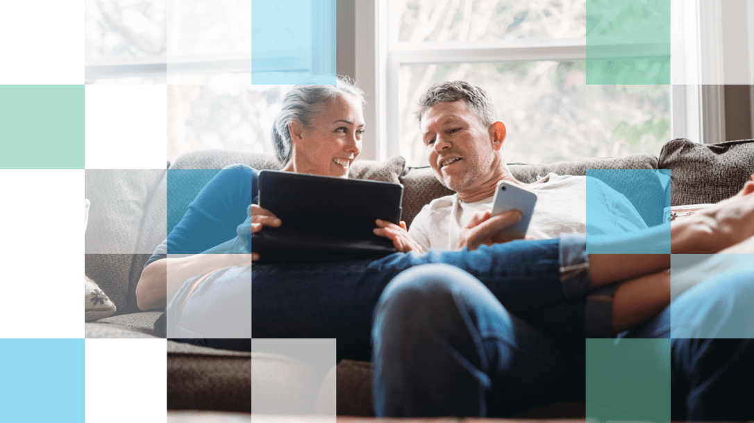 Older man and woman sitting on the couch with mobile and tablet technology smiling